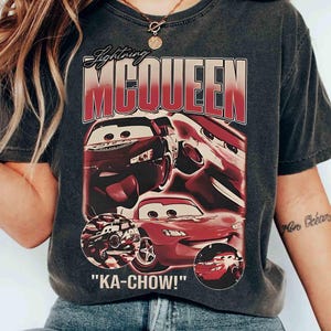 K&ouml;nnte beinhalten: Dunkelgraues T-Shirt mit Lightning McQueen aus dem Film Cars. Das Design zeigt das Bild der Figur und den Schriftzug "KA-CHOW!" in roter und wei&szlig;er Schrift. Das T-Shirt hat einen Vintage-Look.