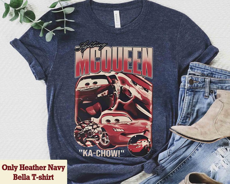 K&ouml;nnte beinhalten: Heather-Marineblaues Bella T-Shirt mit einem Aufdruck von Lightning McQueen aus dem Film Cars. Das Design enth&auml;lt den Text "Lightning McQueen" und "KA-CHOW!" in Rot und Wei&szlig;, mit Bildern des Autos.