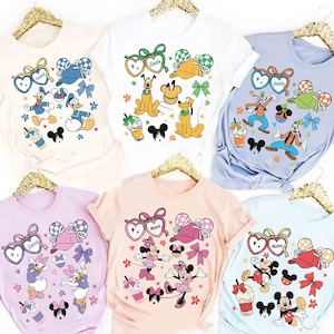 May include: Six t-shirts in various colors, each featuring a different Disney character design. The designs include characters like Donald Duck, Goofy, Minnie Mouse, and Mickey Mouse, along with related accessories and floral accents.