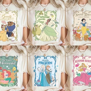 K&ouml;nnte beinhalten: Sechs cremefarbene T-Shirts mit Disney-Prinzessinnen-Grafiken. Designs sind "Die Sch&ouml;ne und das Biest", "Die Prinzessin und der Frosch", "Schneewittchen", "Arielle, die Meerjungfrau", "Frozen" und "Dornr&ouml;schen". Jede Grafik ist mit dekorativen Rahmen versehen.