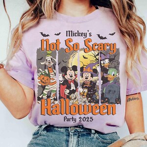 May include: A light purple t-shirt featuring a Halloween design with the text "Mickey's Not So Scary Halloween Party 2025". The graphic includes Disney characters dressed in Halloween costumes, with bats and a full moon.