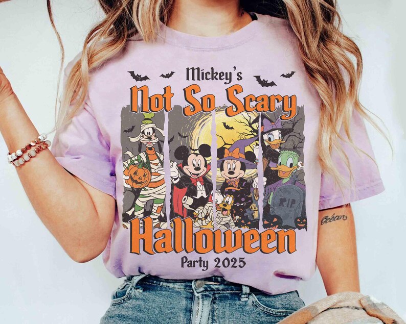 May include: A light purple t-shirt featuring a Halloween design with the text "Mickey's Not So Scary Halloween Party 2025". The graphic includes Disney characters dressed in Halloween costumes, with bats and a full moon.