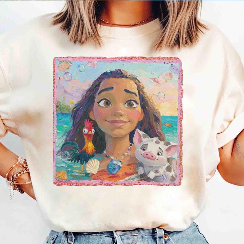 Puede incluir: Una camiseta de color crema con un estampado gr&aacute;fico cuadrado de una persona joven con cabello largo y oscuro, un gallo colorido y un peque&ntilde;o cerdo manchado. La escena se sit&uacute;a sobre un fondo de oc&eacute;ano azul con un borde de color rosa.