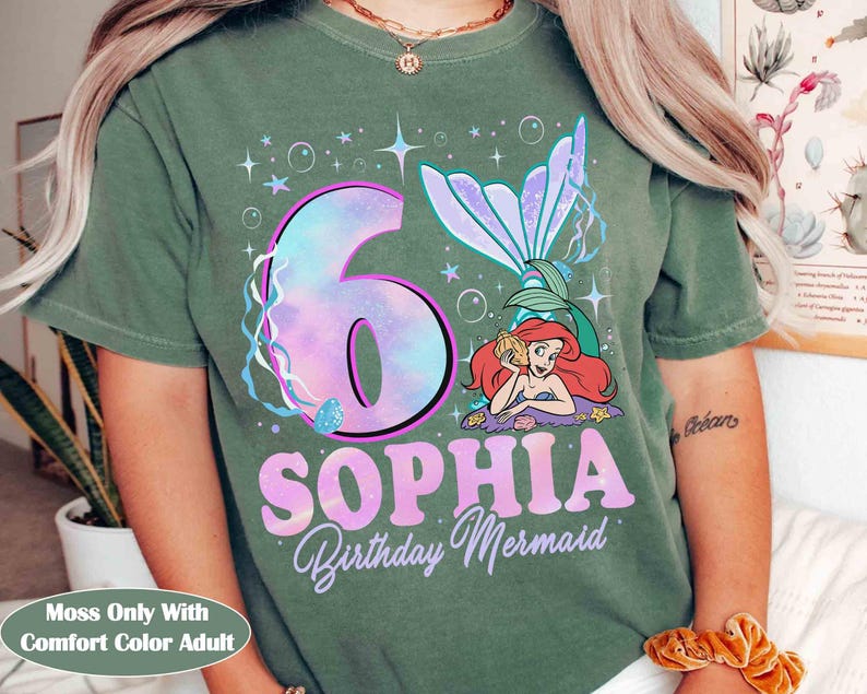 Puede incluir: Camiseta verde con un dise&ntilde;o de sirena. El dise&ntilde;o incluye el n&uacute;mero 6 en un estilo tie-dye, el nombre "Sophia" y las palabras "Birthday Mermaid". Tambi&eacute;n aparece una sirena de dibujos animados.