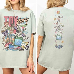 Op de afbeelding: Een lichtgroen t-shirt met Toy Story-personages op de voor- en achterkant. De voorkant toont Jessie, Woody, Buzz, Slinky Dog en anderen met de tekst Toy Story, Since 1995 en Hi. De achterkant toont een verticale rangschikking van personages.