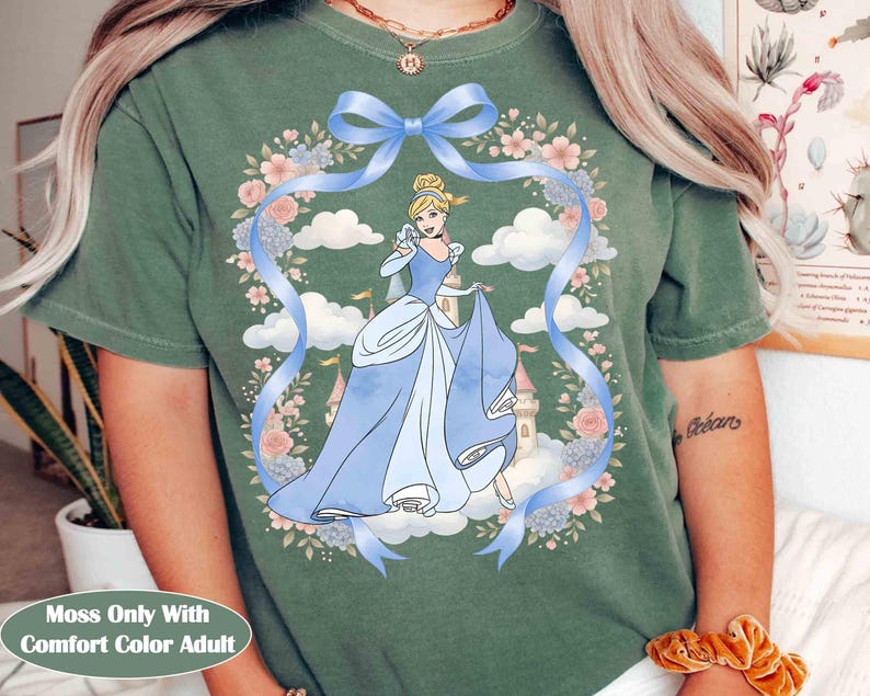May include: Moss green Comfort Color adult t-shirt with a Cinderella graphic. The design features a blue ribbon, floral wreath, and a cartoon image of Cinderella in a blue gown. The text "Moss Only With Comfort Color Adult" is at the bottom.