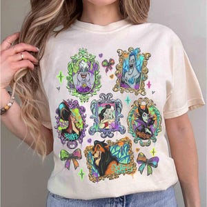 Puede incluir: Camiseta color crema con retratos enmarcados y coloridos de villanos de Disney. Cada retrato tiene un dise&ntilde;o &uacute;nico con acentos de estilo grafiti, lazos y detalles en forma de estrella. La camiseta muestra personajes como &Uacute;rsula, Mal&eacute;fica y Scar.