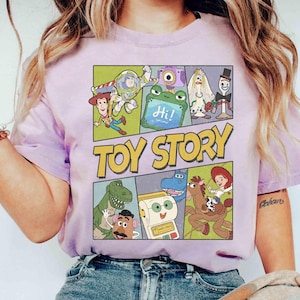 Puede incluir: Una camiseta lila claro con un dise&ntilde;o gr&aacute;fico colorido de personajes de la pel&iacute;cula "Toy Story". El dise&ntilde;o presenta las palabras "Toy Story" en amarillo y personajes de dibujos animados en paneles separados, como un c&oacute;mic.