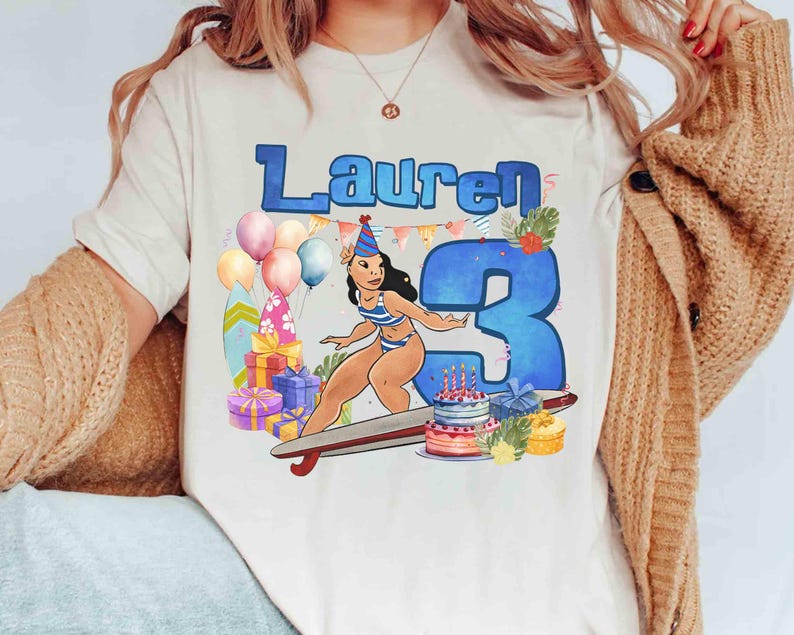 Puede incluir: Camiseta color crema con una ilustraci&oacute;n de dibujos animados para un cumplea&ntilde;os. El dise&ntilde;o incluye el nombre "Lauren" en azul, un gran n&uacute;mero "3" azul, un personaje de dibujos animados en traje de ba&ntilde;o, globos, regalos y una tarta de cumplea&ntilde;os.