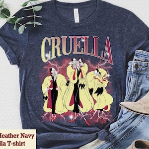Pu&ograve; includere: T-shirt Heather Navy Bella con grafica di Crudelia De Mon e la scritta "Cruella" in giallo e rosso. Il design include un'illustrazione di Crudelia con cappotto giallo e abito nero.
