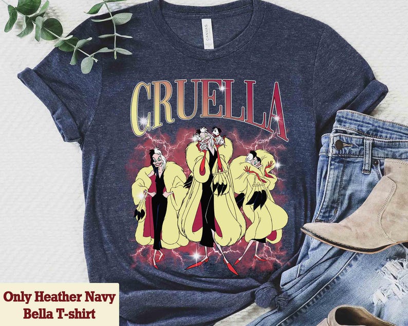 Pu&ograve; includere: T-shirt Heather Navy Bella con grafica di Crudelia De Mon e la scritta "Cruella" in giallo e rosso. Il design include un'illustrazione di Crudelia con cappotto giallo e abito nero.