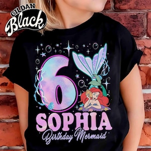 Puede incluir: Camiseta negra con un dise&ntilde;o de sirena. El gr&aacute;fico incluye un gran n&uacute;mero "6" en colores pastel, el nombre "SOPHIA" y las palabras "Birthday Mermaid". El dise&ntilde;o tambi&eacute;n presenta una cola de sirena y una sirena de dibujos animados.