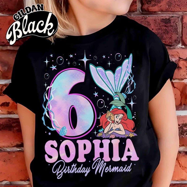 Puede incluir: Camiseta negra con un dise&ntilde;o de sirena. El gr&aacute;fico incluye un gran n&uacute;mero "6" en colores pastel, el nombre "SOPHIA" y las palabras "Birthday Mermaid". El dise&ntilde;o tambi&eacute;n presenta una cola de sirena y una sirena de dibujos animados.