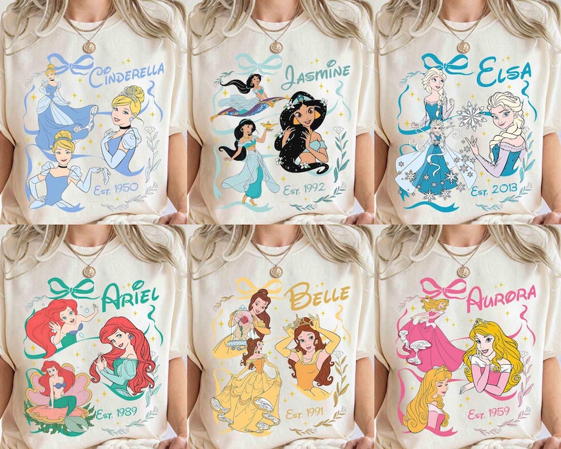 K&ouml;nnte beinhalten: Cremefarbene T-Shirts mit verschiedenen Disney-Prinzessinnen: Cinderella, Jasmin, Elsa, Arielle, Belle und Aurora. Jedes Shirt zeigt den Namen der Prinzessin, Illustrationen und das Jahr ihres Deb&uuml;ts. Die Designs sind mit dekorativen Elementen umrahmt.