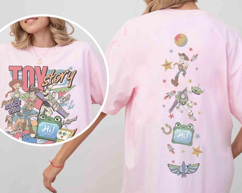 Op de afbeelding: Een lichtroze t-shirt met een Toy Story-afbeelding. De print op de voorkant toont de personages Jessie, Woody, Buzz en anderen met de tekst "TOY story" en "SINCE 1995". De achterkant heeft een verticale opstelling van personages, sterren en een "Hi!"-bord.