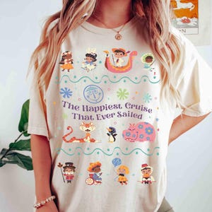 May include: Cream-colored t-shirt featuring a colorful graphic with the text "The Happiest Cruise That Ever Sailed." The design includes cartoon characters, flowers, and a boat. The shirt is a casual, comfortable style.