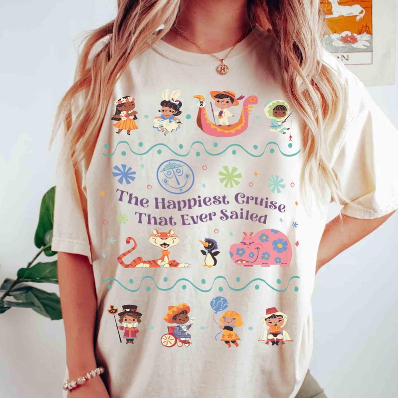 May include: Cream-colored t-shirt featuring a colorful graphic with the text "The Happiest Cruise That Ever Sailed." The design includes cartoon characters, flowers, and a boat. The shirt is a casual, comfortable style.