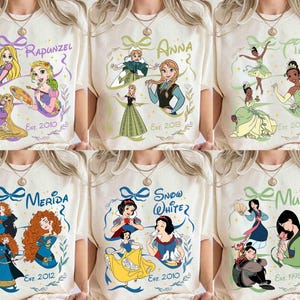 K&ouml;nnte beinhalten: Cremefarbene T-Shirts mit verschiedenen Disney-Prinzessinnen: Rapunzel, Anna, Tiana, Merida, Schneewittchen und Mulan. Jedes Shirt zeigt den Namen der Prinzessin, eine Grafik und das Erscheinungsjahr des Films.