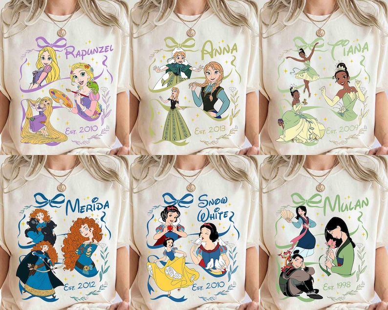 K&ouml;nnte beinhalten: Cremefarbene T-Shirts mit verschiedenen Disney-Prinzessinnen: Rapunzel, Anna, Tiana, Merida, Schneewittchen und Mulan. Jedes Shirt zeigt den Namen der Prinzessin, eine Grafik und das Erscheinungsjahr des Films.