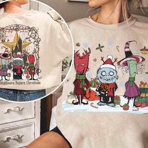 May include: Beige sweatshirt with a colourful graphic from "The Nightmare Before Christmas." The design features characters in festive attire, surrounded by Christmas decorations. The text "The Nightmare Before Christmas" is printed at the bottom of the design.