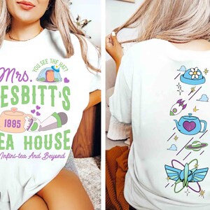 May include: A white t-shirt featuring a front graphic with the text Mrs. Nesbitt's Tea House, 1995, and To Infini-tea And Beyond, alongside a teapot and hat. The back graphic displays a vertical arrangement of a hat, rocket, teapot, planet, and wings.