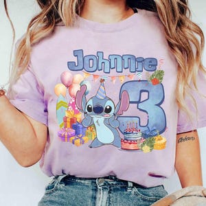 Puede incluir: Camiseta lila claro con un dise&ntilde;o de Stitch, el nombre "Johnnie" y el n&uacute;mero "3". El dise&ntilde;o incluye globos, regalos, una tabla de surf y una tarta de cumplea&ntilde;os. La camiseta es de material suave.
