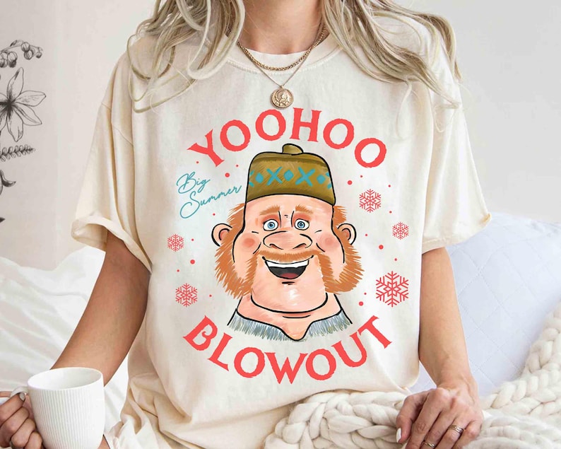 May include: Cream-colored t-shirt featuring a cartoon illustration of a smiling man with a red beard and a hat. The text "YOO HOO BLOWOUT" is printed in red, with "Big Summer" in blue script. Red snowflakes are scattered around the design.