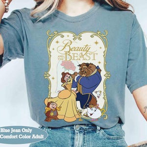 K&ouml;nnte beinhalten: Blaues Jeans-T-Shirt mit einem Grafikmotiv aus Disneys Die Sch&ouml;ne und das Biest. Das Design zeigt Belle, das Biest und andere Charaktere, mit dem Titel in goldener Schrift. Das Shirt ist in Erwachsenengr&ouml;&szlig;e und Comfort Color.