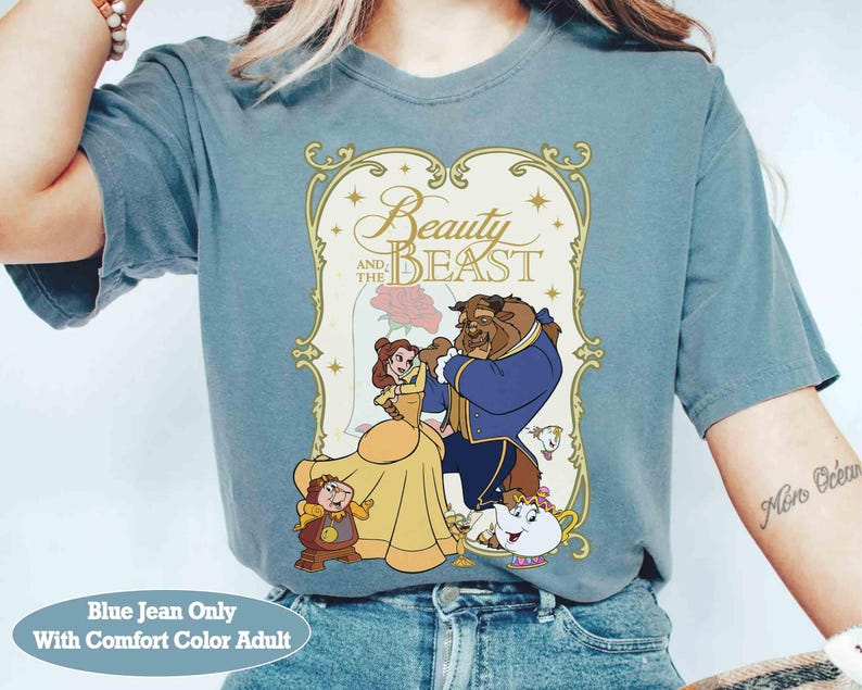 K&ouml;nnte beinhalten: Blaues Jeans-T-Shirt mit einem Grafikmotiv aus Disneys Die Sch&ouml;ne und das Biest. Das Design zeigt Belle, das Biest und andere Charaktere, mit dem Titel in goldener Schrift. Das Shirt ist in Erwachsenengr&ouml;&szlig;e und Comfort Color.