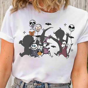 Puede incluir: Camiseta blanca con un dise&ntilde;o tem&aacute;tico de Halloween. El dise&ntilde;o incluye personajes de dibujos animados, murci&eacute;lagos y globos con caras de calaveras y calabazas. Los personajes corren, creando una escena juguetona y festiva.