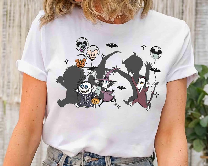 Puede incluir: Camiseta blanca con un dise&ntilde;o tem&aacute;tico de Halloween. El dise&ntilde;o incluye personajes de dibujos animados, murci&eacute;lagos y globos con caras de calaveras y calabazas. Los personajes corren, creando una escena juguetona y festiva.