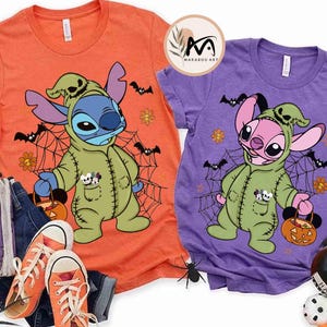 May include: Two short-sleeved t-shirts, one orange and one purple, feature a cartoon character in a green costume holding a pumpkin-shaped basket. The design includes bats, spiderwebs, and flowers, perfect for Halloween.