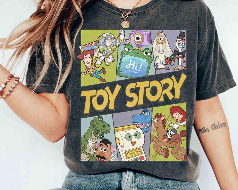 Puede incluir: Camiseta gris oscuro con un dise&ntilde;o colorido de la pel&iacute;cula animada "Toy Story". El dise&ntilde;o incluye personajes como Woody y Buzz Lightyear, con el t&iacute;tulo de la pel&iacute;cula en amarillo. La camiseta tiene un aspecto vintage.