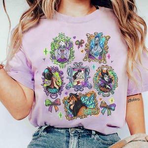 Puede incluir: Una camiseta lila claro con retratos enmarcados de villanos animados. Los retratos est&aacute;n en marcos dorados ornamentados con detalles coloridos. La camiseta tiene cuello redondo y mangas cortas. El dise&ntilde;o incluye lazos y estrellas.