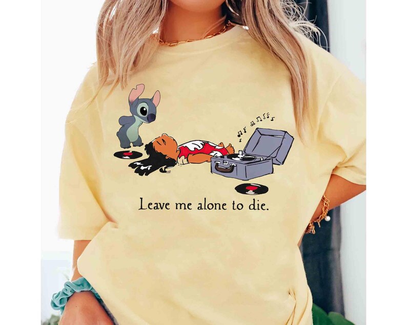 May include: Yellow t-shirt featuring a cartoon illustration of Lilo and Stitch with a record player. The image includes the text "Leave me alone to die."