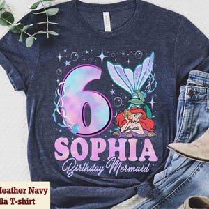 Puede incluir: Camiseta Heather Navy Bella con un dise&ntilde;o de cumplea&ntilde;os de sirena. La camiseta presenta un gran n&uacute;mero 6 con efecto acuarela, el nombre "Sophia" y las palabras "Birthday Mermaid". Tambi&eacute;n aparece una sirena de dibujos animados.