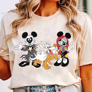 May include: Beige t-shirt featuring cartoon characters in Halloween costumes. Jack Skellington, a ghost-like dog, and Sally are depicted in a playful, colorful design. The shirt is a casual, comfortable style.