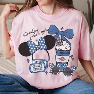 May include: Pink t-shirt with the text "literally just a girl" and graphic designs. The graphics include Minnie Mouse ears, sunglasses, a coffee cup, and cruise tickets. The Minnie Mouse ears and sunglasses have a blue and white polka dot pattern.