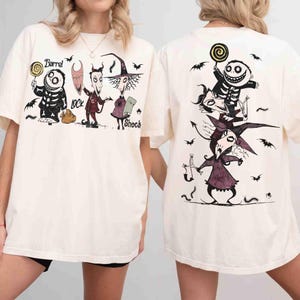 Puede incluir: Una camiseta color hueso con estampados gráficos de los personajes Barrel, Lock y Shock de Pesadilla antes de Navidad. El frente muestra a los personajes de pie uno al lado del otro con sus nombres, mientras que la espalda los muestra apilados.