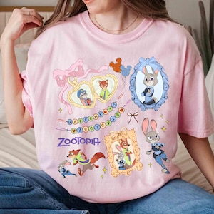 Puede incluir: Camiseta rosa claro con personajes de Zootopia y el texto "WELCOME TO ZOOOTPIA". El dise&ntilde;o incluye retratos enmarcados de Judy Hopps y Nick Wilde, junto con otros personajes y elementos decorativos.