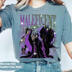Pu&ograve; includere: T-shirt blu jeans con grafica di Malefica, un drago e la scritta "Maleficent". Il design include elementi viola, neri e verdi. La maglietta &egrave; una taglia adulto comfort.