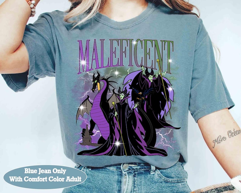 Pu&ograve; includere: T-shirt blu jeans con grafica di Malefica, un drago e la scritta "Maleficent". Il design include elementi viola, neri e verdi. La maglietta &egrave; una taglia adulto comfort.