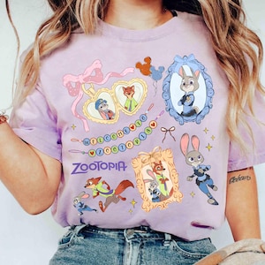 Puede incluir: Camiseta lila claro con personajes de Zootopia y el texto "WELCOME TO ZOOTOPIA". El dise&ntilde;o incluye retratos enmarcados de Judy Hopps y Nick Wilde, junto con otros gr&aacute;ficos de Zootopia.