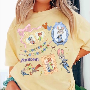 Puede incluir: Camiseta amarilla clara con ilustraciones de dibujos animados de personajes de la pel&iacute;cula Zootopia. El dise&ntilde;o incluye retratos enmarcados de Judy Hopps y Nick Wilde, y el texto "WELCOME TO ZOOTOPIA".
