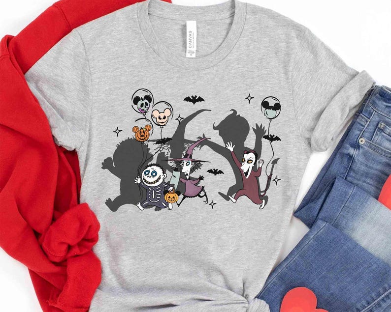 Puede incluir: Una camiseta gris claro con un dise&ntilde;o de dibujos animados de Halloween. El gr&aacute;fico representa varios personajes, incluyendo un esqueleto, una bruja y un vampiro, con globos y murci&eacute;lagos. La camiseta est&aacute; hecha de un material suave.