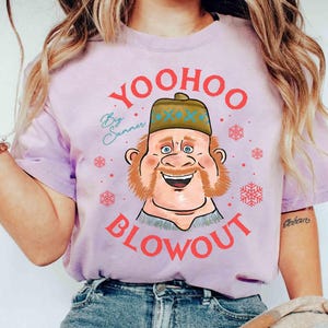 May include: A light purple t-shirt featuring a cartoon illustration of a smiling man with a beard and hat. The text "Yoohoo Blowout" is in red, with "By Summer" in cursive. Snowflake graphics are also present.