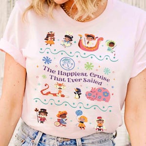 May include: Light pink t-shirt featuring a colorful graphic with the text "The Happiest Cruise That Ever Sailed." The design includes cartoon characters, a tiger, a hippo, and other whimsical elements. The shirt has short sleeves and a crew neck.