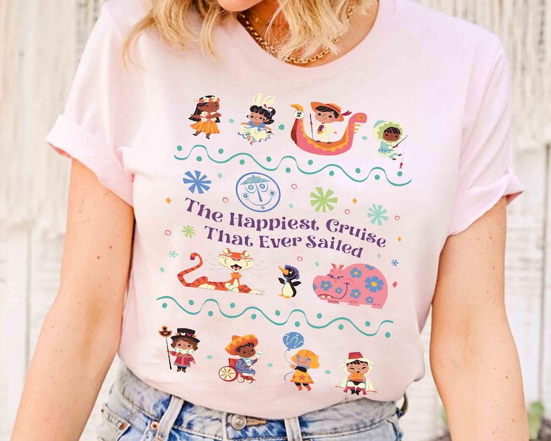 May include: Light pink t-shirt featuring a colorful graphic with the text "The Happiest Cruise That Ever Sailed." The design includes cartoon characters, a tiger, a hippo, and other whimsical elements. The shirt has short sleeves and a crew neck.