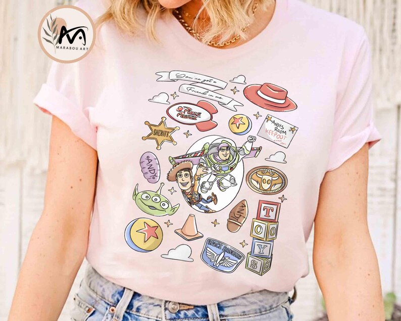 May include: Light pink t-shirt featuring a colorful graphic design with characters and elements from the animated film "Toy Story." The design includes Woody, Buzz Lightyear, and other iconic imagery. The text "Don't you get it? Friend in me" is also visible.