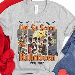 May include: A gray t-shirt featuring a Halloween design with Disney characters. The design includes Mickey Mouse, Minnie Mouse, Donald Duck, and Goofy in Halloween costumes. The text reads "Mickey's Not So Scary Halloween Party 2025".